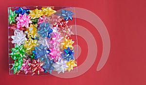 Box with colorful ornament bows on red background. Copy space