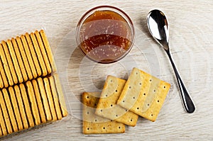 Box with crackers, bowl with apple jam, spoon, cookies on wooden table. Top view