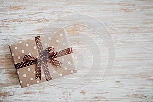 Box in craft paper, eco paper on the wooden table. Top view. Brown paper wrapped gift box with satin ribbon bow on a old