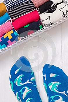 Box with different colorful socks. Feet selfie and a socks organizer on a white wooden background. Top view