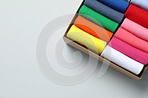 Box with different colorful socks on light background, top view. Space for text