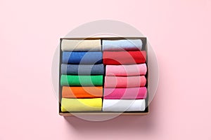 Box with different colorful socks on light pink background, top view