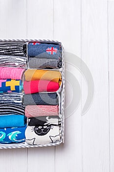 Box with different colorful socks on a white wooden background.Top view, free space