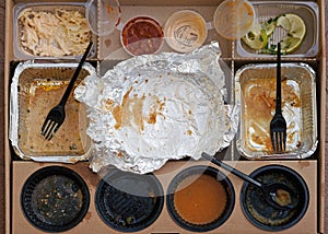 Box of fast food, empty plates with forks, sauces and aluminum bowls top view.