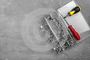 box with fasteners and two screwdrivers on grey wooden background. repair, tools