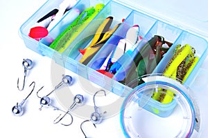 Box for fishing accessories with silicone baits inside, Jig hooks, braided reel on a white background close-up