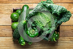 Box with Fresh Organic Green Vegetables Savoy Cabbage Zucchini Cucumbers Bell Peppers Avocados on Aged Plank Wood Background