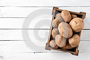 Box of fresh potatoes on white wooden table with copyspace.