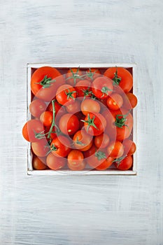 Box of fresh ripe red tomatoes in different sizes on white wood kitchen table