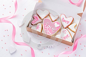 A box full of heart shaped cookies with glazed word love near the key on white wood table