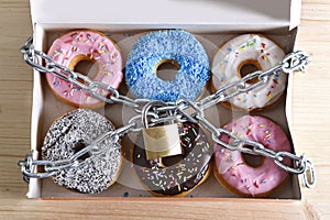 Box full of tempting delicious donuts wrapped in metal chain and lock in sugar and sweet addiction photo