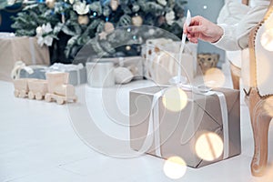 Box with Luxury Metallics gift on background of Christmas tree. Hands open New Year`s gift close-up, copy space