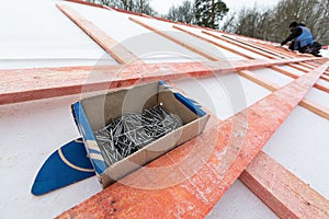 The box with nails on the roof and roofer working on roof structure of building on construction site