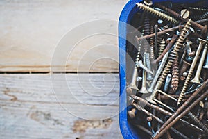 Box of old rusty metal screws on wooden background