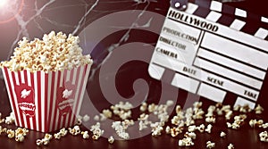 A box of popcorn stands on a wood table. Behind the box, there is a clapperboard in the blurry background.