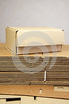 Box ready for product packaging and a stack of folded corrugated cardboard sheets on a table