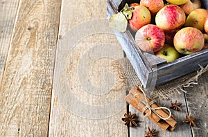 Box with ripe apples and cinnamom on wooden background