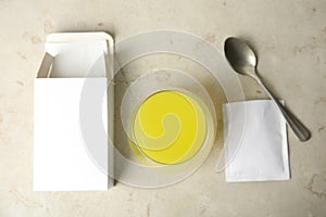 Box with sachets, spoon and glass of dissolved medicine on light background, flat lay