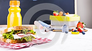 Box with school lunch near the black board. Healthy food for a child. Toast with salad and strawberries and blueberries