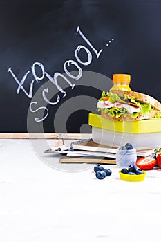 Box with school lunch near the black board. Healthy food for a child. Toast with salad and strawberries and blueberries