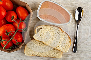 Box with tomatoes, opened jar with liver pate, slices bread, spoon on wooden table. Top view