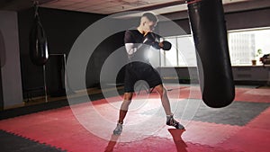 Box training - aggressive sportsman wearing boxing gloves punching the punching bag in the gym