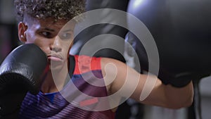 box training of young afro-american guy, handsome young man is punching by hands punching bag