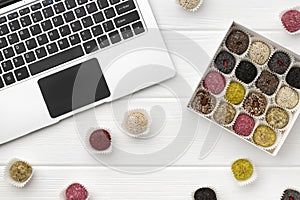 Box of vegan sweets energy balls near the laptop on white wooden table