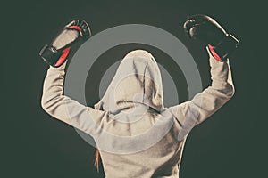 Boxer in hoodie stand backwards with arms in air.