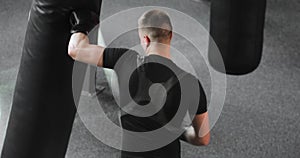 Boxer man in gloves making blows on punching bag boxing in gym, back view.