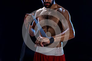 Boxer preparing her gloves for a fight. Photo of muscular man strapping up hands on black background.