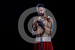 Boxer preparing her gloves for a fight. Photo of muscular man strapping up hands on black background.