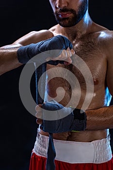 Boxer preparing her gloves for a fight. Photo of muscular man strapping up hands on black background.