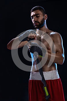 Boxer preparing her gloves for a fight. Photo of muscular man strapping up hands on black background.