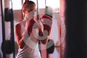 Boxer training her fitness in the gym using a punching bag practicing for a fight competition. Active, wellness and fit