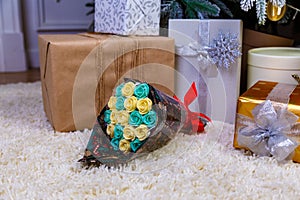 boxes with Christmas gifts under the blue Christmas tree, in foreground a bouquet of chocolate flowers