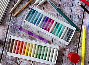 The boxes contain a set of pastels. Felt pens, pencils and other items lie on a wooden table.