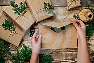 Boxes packed in kraft paper, green branches on a wooden background. Women`s hands hold an envelope