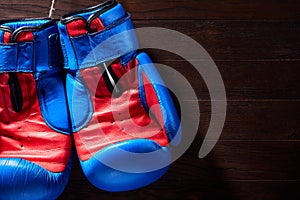 Boxing blue and red gloves hanging from ropes on a wooden background.