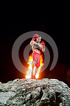 Boxing champion posing on top of a rock with fire burning on the
