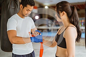 a boxing coach helping the female boxer to wearing the boxing gloves