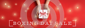 Boxing day sale banner design. Woman holding gift on red background