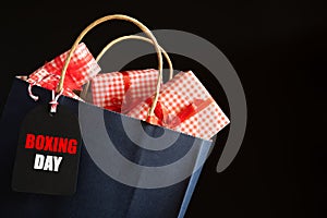 Boxing day Sale text on a black tag with shopping bag and gift box on black background. Online Shopping