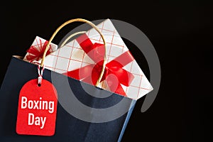 Boxing day Sale text on a black tag with shopping bag and gift box on black background. Online Shopping