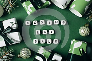 Boxing day sale text on green background. Wrapped gift boxes and fir tree branches. Top view, flat lay. Christmas sale concept