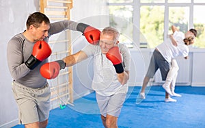 Boxing fight - elderly man learning to box in sparring with trainer in gym