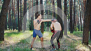 In boxing gloves, young athletic men with bare, naked torsos, box, practice the technique of strikes, capture, fight