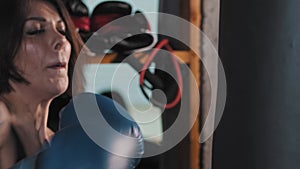 Boxing in the gym - a tattooed woman punching the punching bag with an effort wearing boxer gloves