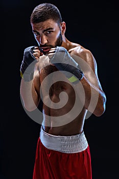 Boxing man ready to fight. Boxer with strong hands and clenched fists in blue straps against a black background