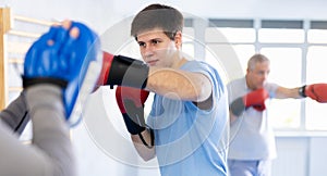 Boxing training - young guy masters boxing strikes on trainer punch mitts during training